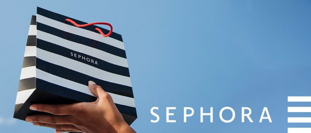 Visuel de la marque Sephora montrant une main tenant un sac de shopping rayé noir et blanc avec le logo Sephora. L’image est placée sur un fond bleu ciel épuré, avec le nom Sephora affiché en grandes lettres blanches sur la droite. Elle illustre l’univers de la beauté, du maquillage, du parfum et des soins proposés par l’enseigne.